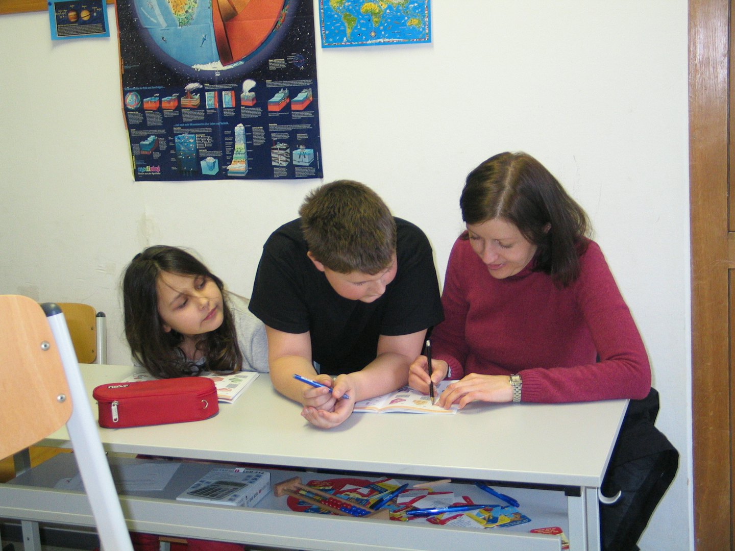 Teacher helps two children with an activity at a desk.