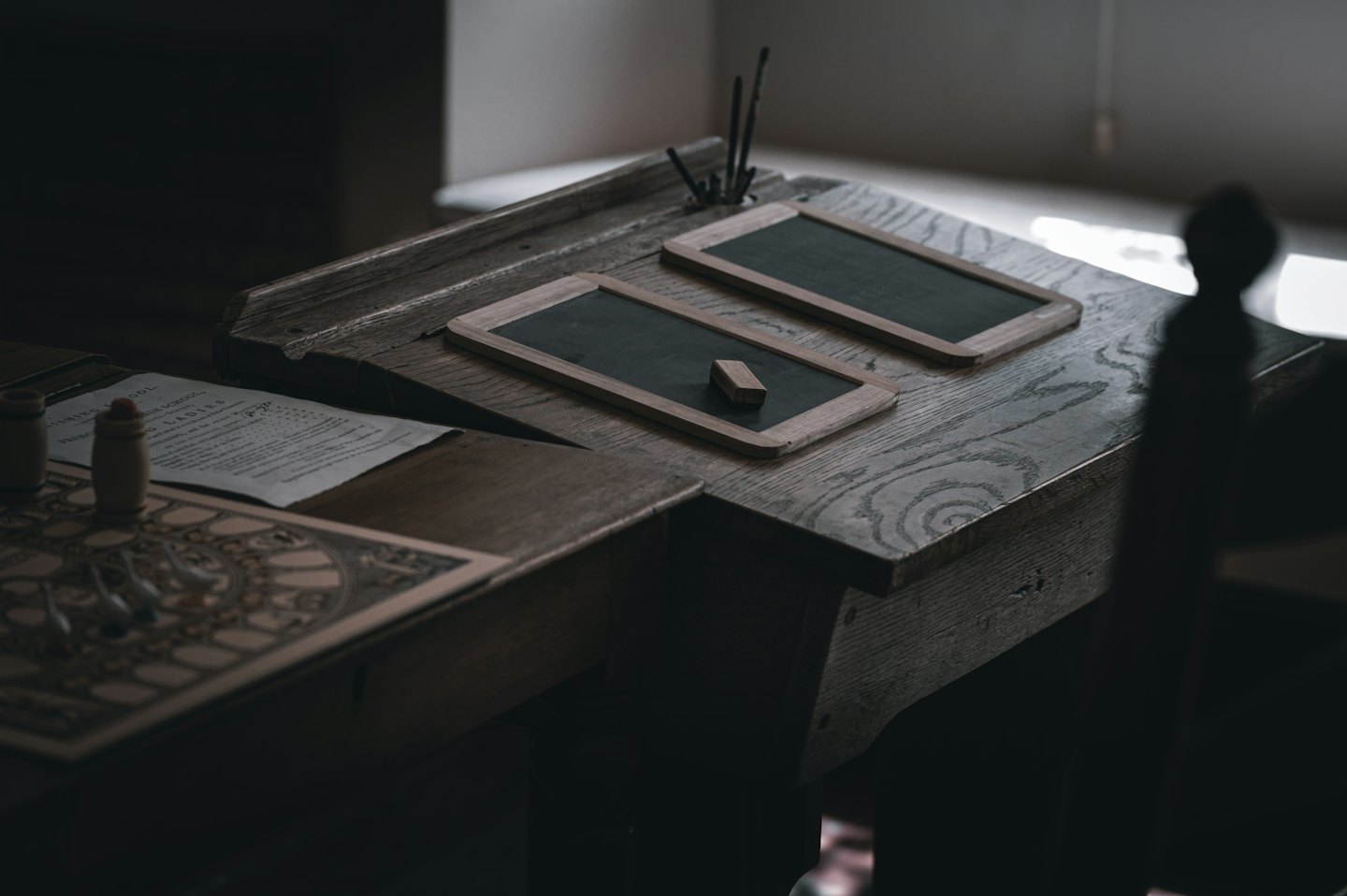 Vintage wooden school desk displays chalkboards, an eraser, and papers.